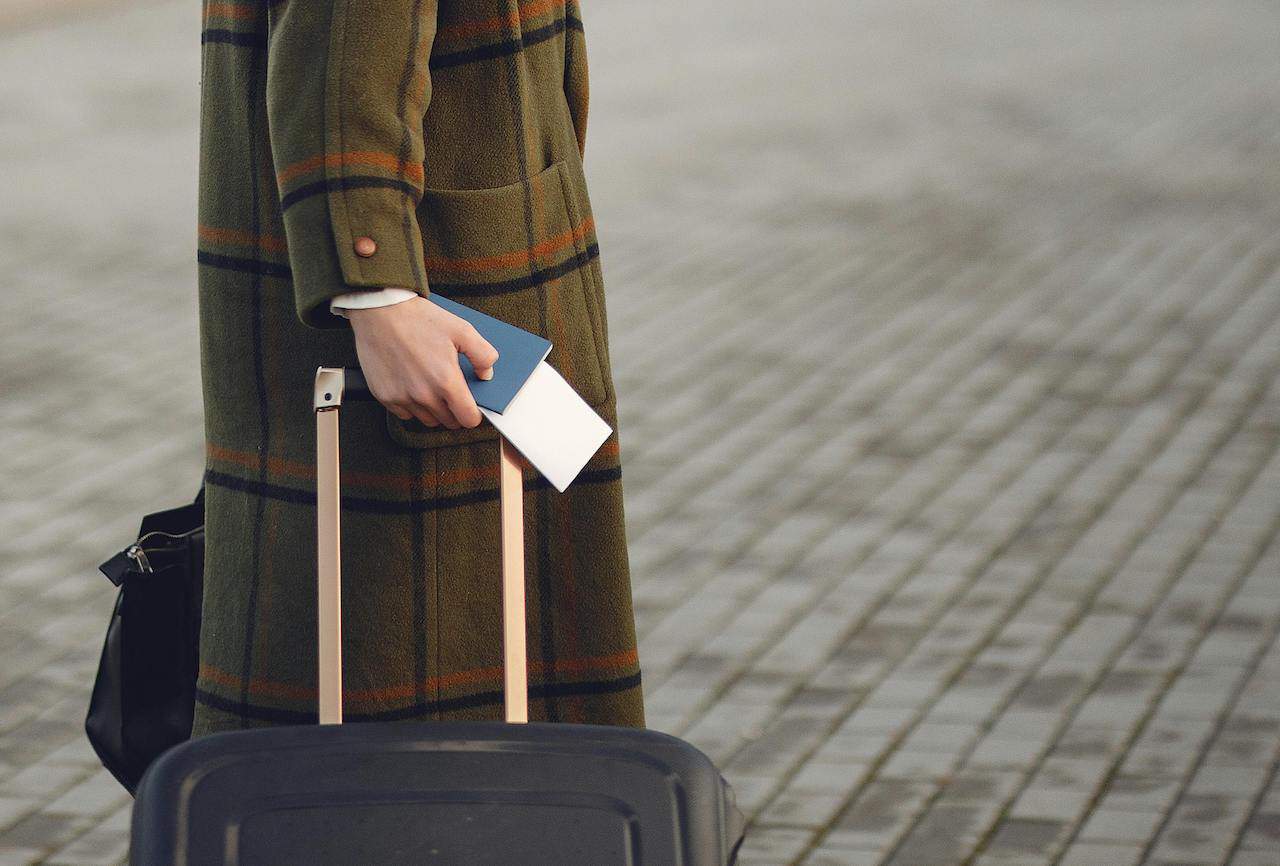 Woman carrying passport and wheeling bag.