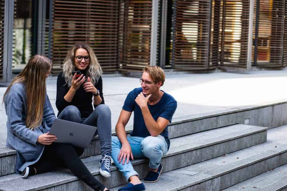 Three students sitting on university steps. AI.