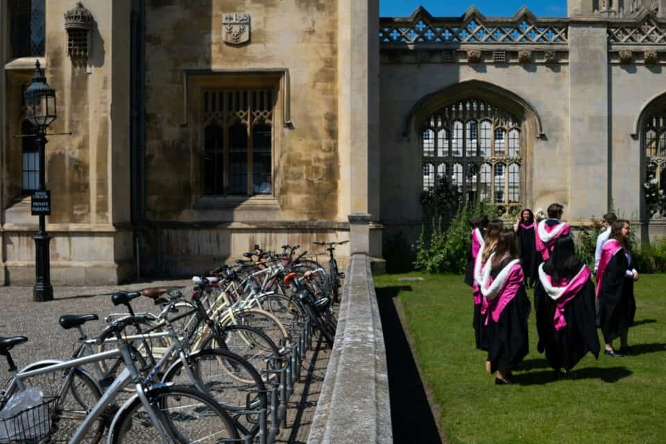 Graduates wearing gowns walk on university campus, beside a row of bikes