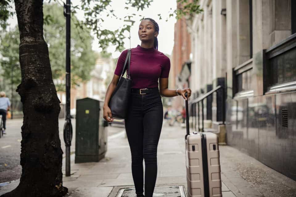 A woman is walking around London wearing a purple sweater and carrying a bag