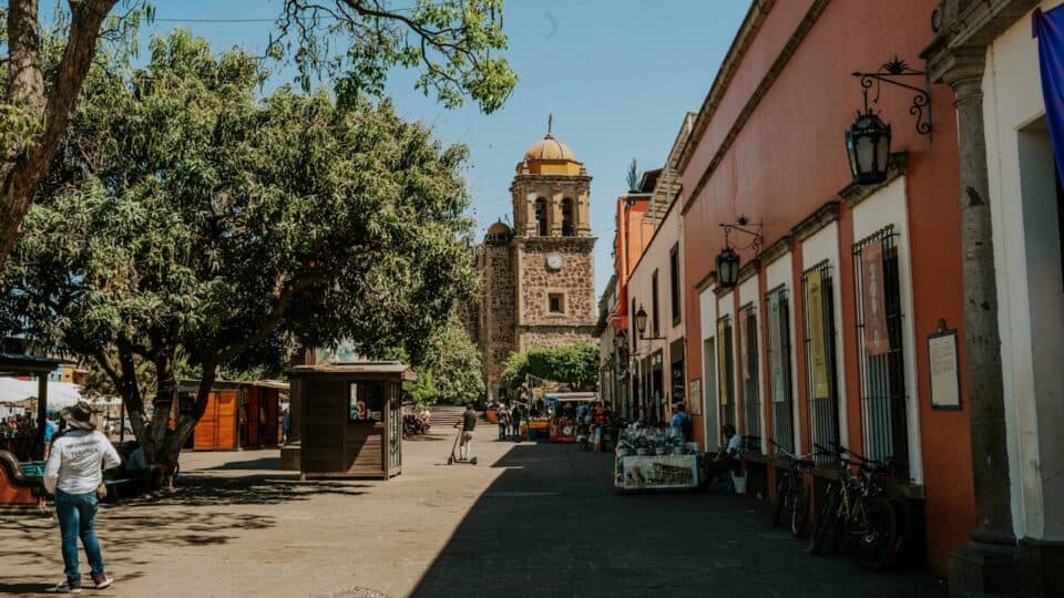 Road in Mexico City with buildings, trees and a church at the end.