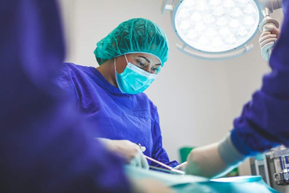 A dentist wears a hair net and mask and works on a patient