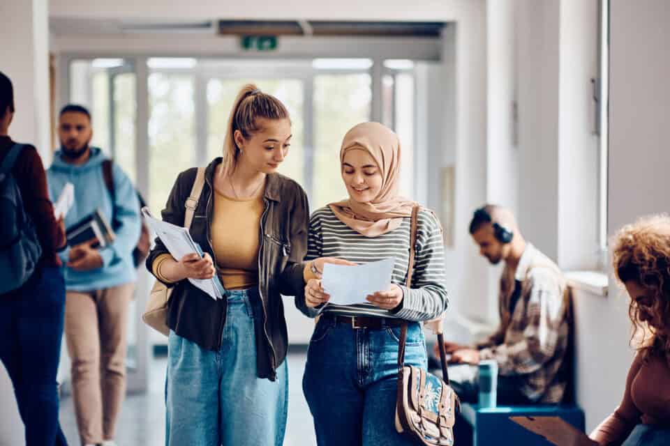 Two female university students walking down corridor.