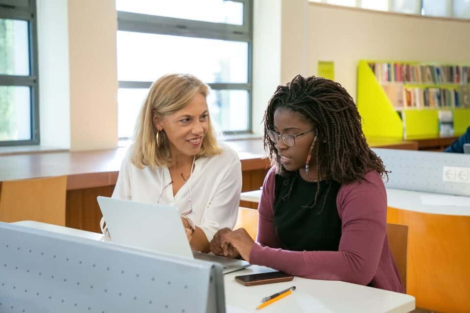 Teacher sitting with adult student in classroom.