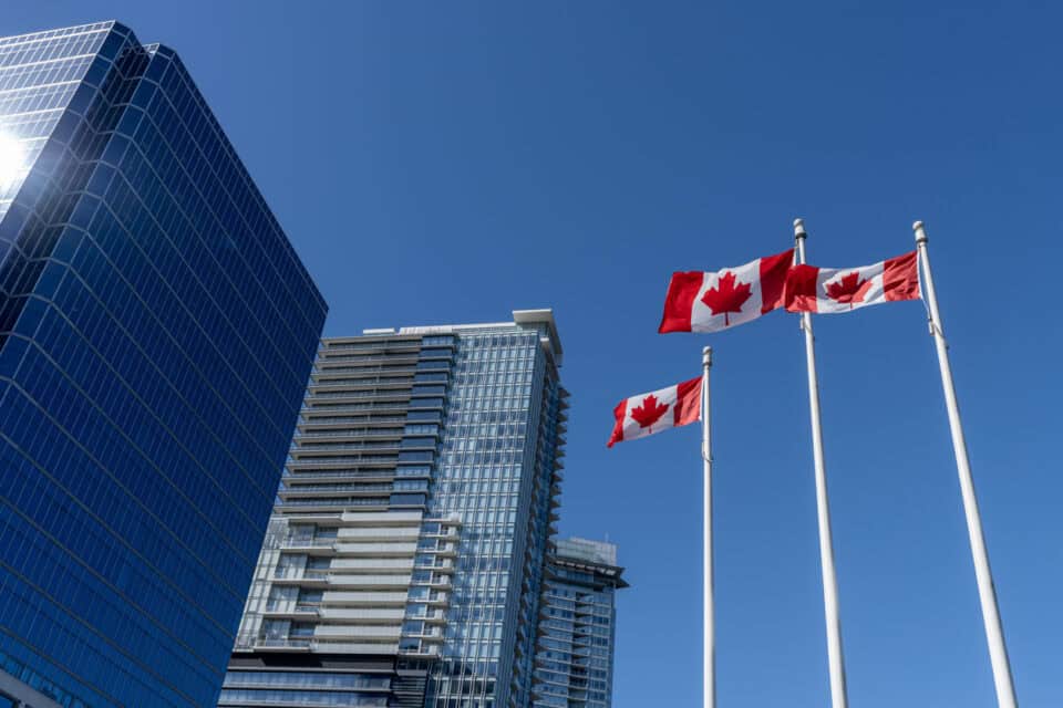 Three Canadian flags next to buildings against a blue sky.