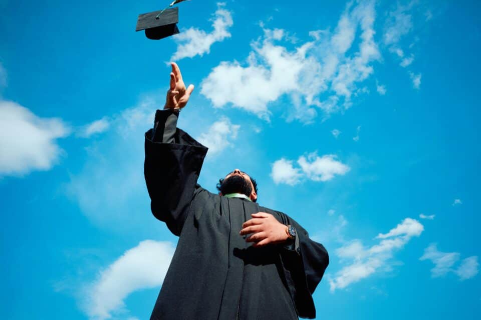 Student throws graduation hat in the air against blue sky